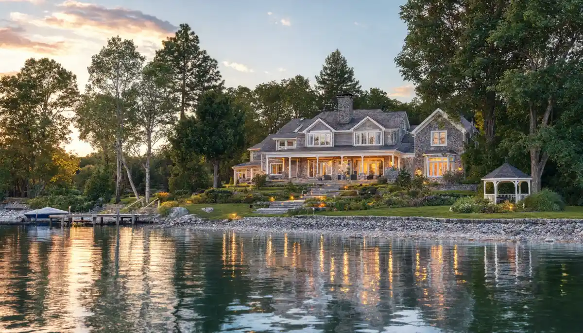 Private lakeside Michigan estate with a luxury waterfront home, landscaped gardens, covered porch, private dock, and peaceful shoreline surrounded by mature trees at sunset.