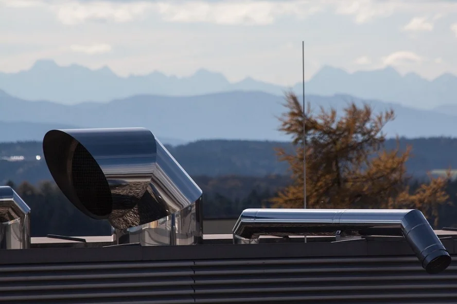 Metal air duct pipes on a rooftop with a scenic mountain backdrop.