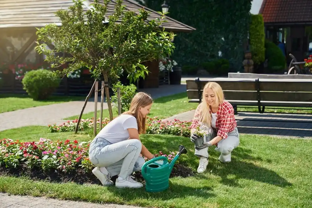 Two women planting flowers and watering plants for perfect lawn care.